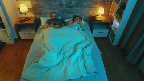 Top-view-of-couple-in-the-bedroom-late-at-night-using-their-phones