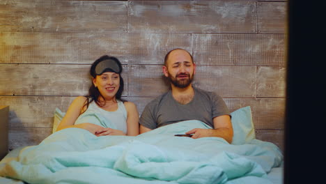 Amused-couple-watching-TV-in-bedroom