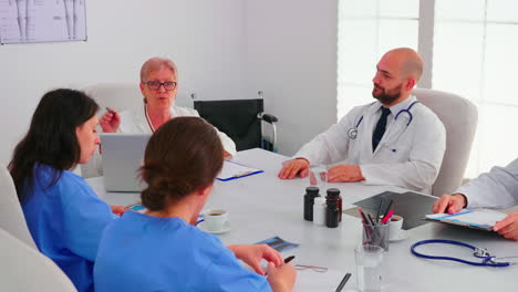 Mature-doctor-presenting-health-report-during-meeting-with-coworkes