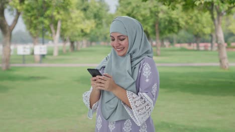 Happy-Muslim-woman-typing-on-phone-in-park