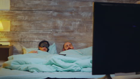 Couple-in-bedroom-falling-asleep-in-front-of-tv