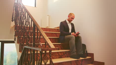 Hombre-De-Negocios-Escribiendo-En-Un-Teléfono-Inteligente-Sentado-En-Las-Escaleras