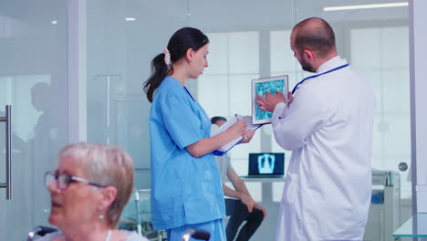 Personal-Médico-Sosteniendo-Una-Tableta-Con-Radiografía-Del-Paciente-En-El-Pasillo-Del-Hospital