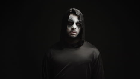 Young-man-dressed-up-like-grim-reaper-over-black-background