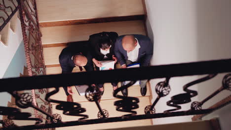 Top-view-of-project-team-looking-on-documents-sitting-on-stairs