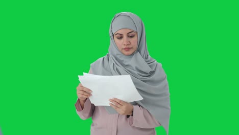 Muslim-businesswoman-reading-reports-in-office-Green-screen