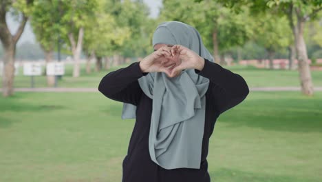 Glückliche-Muslimische-Frau-Zeigt-Herzschild-Im-Park