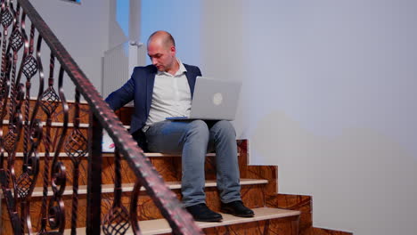 Businessman-on-stairs-writing-on-laptop-overtime