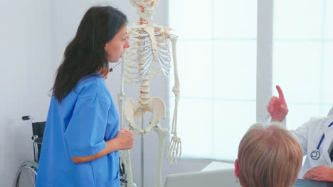 Female-nurse-demonstrating-on-skeleton-in-front-of-medical-surgeons
