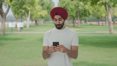Happy-Sikh-Indian-man-texting-someone-in-park