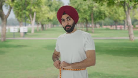 Feliz-Hombre-Indio-Sikh-Midiendo-La-Cintura-Usando-Cinta-De-Pulgada-En-El-Parque