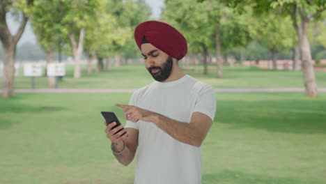 Cansado-Y-Somnoliento-Hombre-Indio-Sikh-Desplazando-El-Teléfono-En-El-Parque