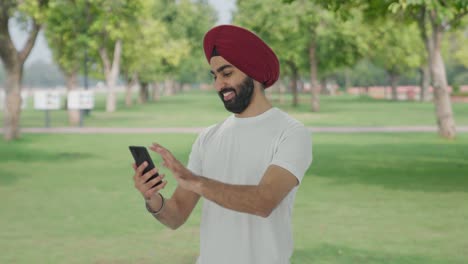 Happy-Sikh-Indian-man-scrolling-phone-in-park