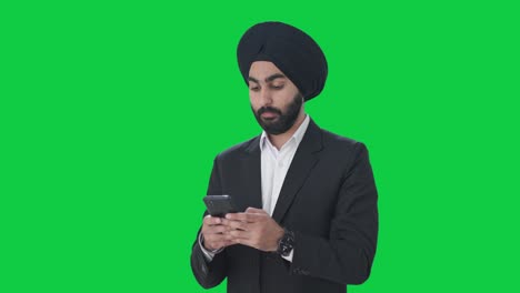 Ernsthafter-Indischer-Sikh-Geschäftsmann,-Der-Jemandem-Eine-SMS-Auf-Grünem-Bildschirm-Schreibt