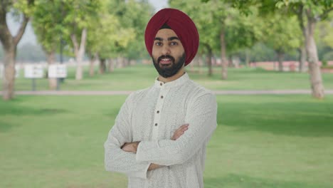 Portrait-of-Happy-Sikh-Indian-man-standing-crossed-hands-in-park