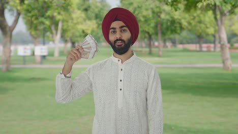 Egoistischer-Sikh-Indianer,-Der-Geld-Als-Fächer-Mit-Listigem-Lächeln-Im-Park-Verwendet