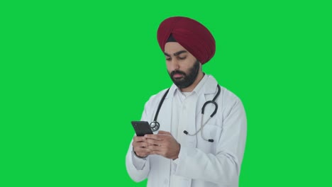 Ernsthafter-Indischer-Sikh-Arzt,-Der-Jemandem-Eine-Nachricht-Auf-Grünem-Bildschirm-Sendet