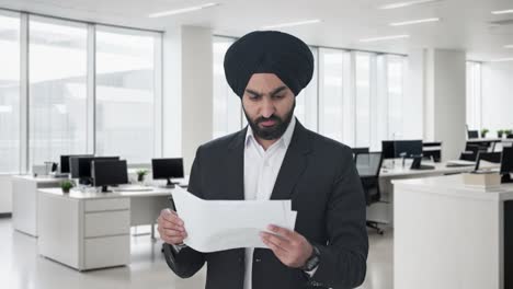 Betonter-Sikh-indischer-Geschäftsmann,-Der-Unternehmensberichte-Liest