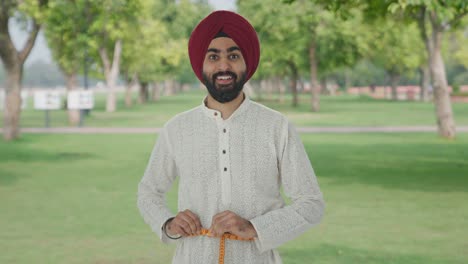 Happy-Sikh-Indian-man-measuring-waist-using-inch-tape-in-park