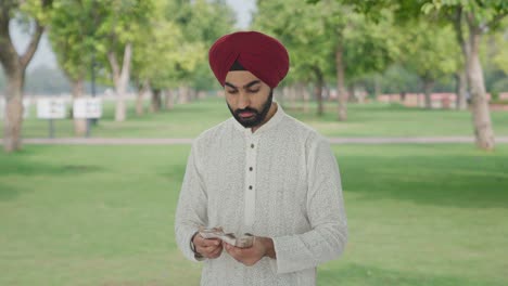 Sad-Sikh-Indian-man-counting-money-in-park