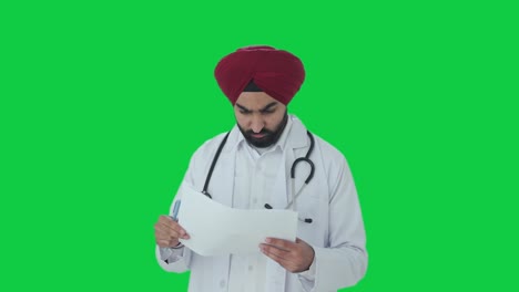 Seriöser-Indischer-Sikh-Arzt-überprüft-Medizinische-Berichte-Auf-Grünem-Bildschirm