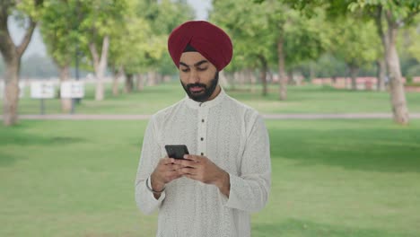 Glücklicher-Sikh-Indianer,-Der-Jemandem-Im-Park-Eine-SMS-Schreibt
