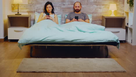 Bored-young-couple-in-pajamas-using-smartphone