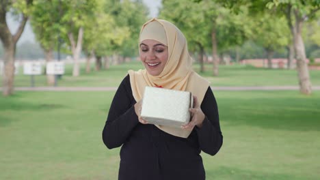 Glückliche-Muslimische-Frau,-Die-Im-Park-Ein-Geschenk-Erhält