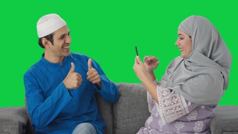 Glückliche-Muslimische-Frau,-Die-Auf-Bilder-Ihres-Mannes-Auf-Grünem-Bildschirm-Klickt