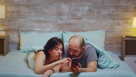 Husband-and-wife-using-phone-while-laying-in-bed