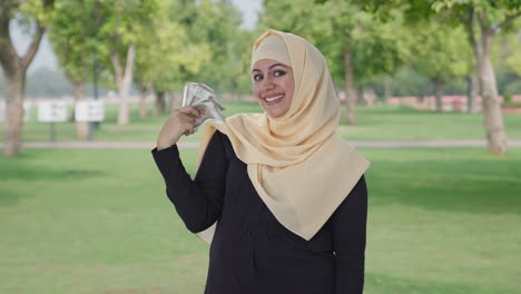 Glückliche-Muslimische-Frau,-Die-Geld-Als-Fächer-Im-Park-Verwendet