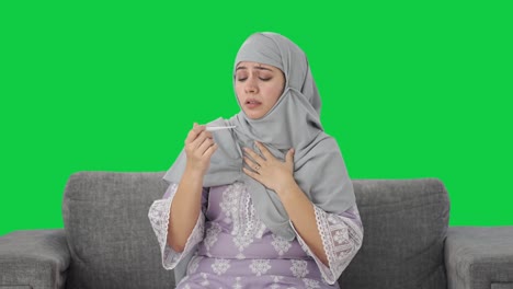 Mujer-Musulmana-Enferma-Controlando-La-Fiebre-Usando-Un-Termómetro-De-Pantalla-Verde
