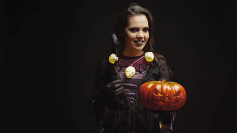 Smiling-witch-holding-pumpkin-over-black-background