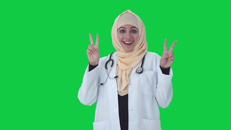 Fröhlicher-Muslimischer-Arzt-Zeigt-Siegeszeichen-Auf-Grünem-Bildschirm