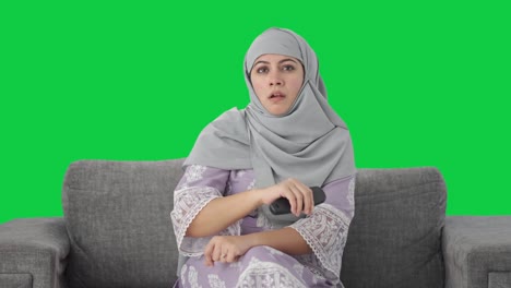 Ernsthafte-Muslimische-Frau,-Die-Zu-Hause-Fernsieht,-Grüner-Bildschirm