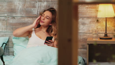 Zoom-in-shot-of-tired-woman-in-pajamas-using-her-smartphone