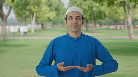 Concentrated-Muslim-man-doing-breathe-in-breathe-out-exercise-in-park