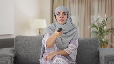 Mujer-Musulmana-Enojada-Tratando-De-Arreglar-El-Control-Remoto-De-La-Televisión