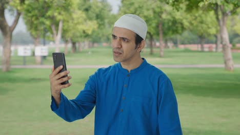 Hombre-Musulmán-Enojado-Hablando-Por-Videollamada-En-El-Parque