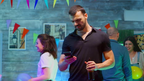 Bored-millennial-man-using-his-smartphone-while-his-friends-are-partying-wild
