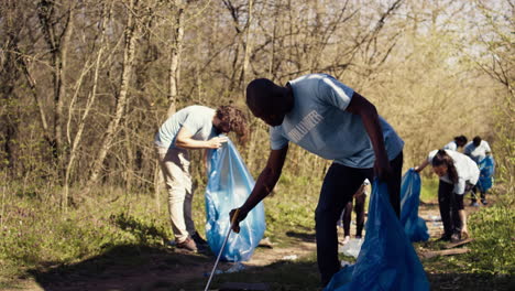 African-american-man-volunteer-collecting-trash-and-plastic-waste-with-tongs