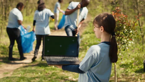 Little-child-holding-a-laptop-with-isolated-greenscreen-in-the-woods