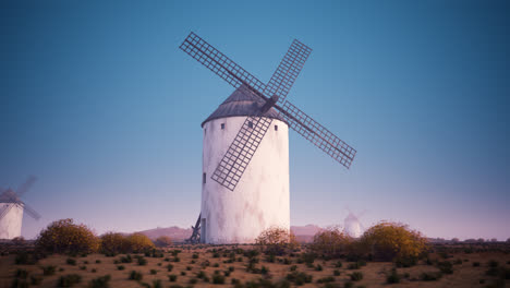 Vintage-agriculture-windmill’s-wings-working-and-rotating-slowly-during-sunset-with-clouds-in-the-background.-Camera-slowly-pans-around-a-building.-Spinning-turbine,-old-technology,-an-energy-exchange