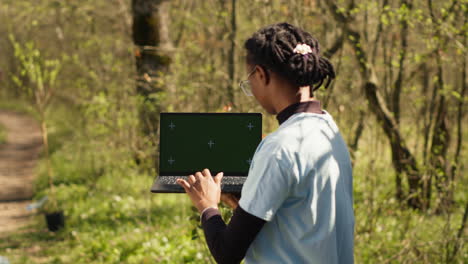 African-american-girl-cleaning-up-forest-and-using-isolated-laptop-display