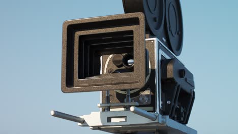 Alte,-Retro-Vintage-Filmkamera-Mit-Einem-Klaren,-Blauen-Himmel-Im-Hintergrund.-Sonnenlicht-Beleuchtet-Eine-Filmspulenhülle,-In-Der-Hollywoods-Filmausrüstung-Steckt.-Die-Kamera-Fährt-Von-Der-Ausrüstung-Zurück.