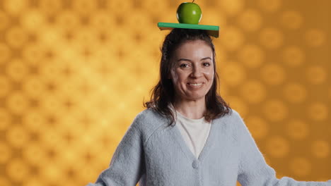 Woman-balancing-book-and-apple-on-head,-acting-zany,-studio-background