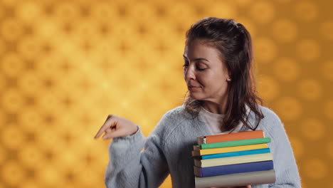 Portrait-of-smiling-woman-holding-pile-of-books-pointing-to-empty-copy-spaces