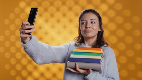 Cheerful-lady-with-stack-of-novels-in-arms-doing-selfies,-studio-background
