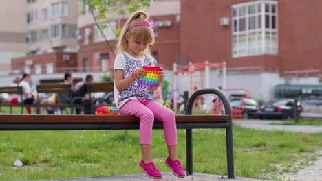Joyful-kid-girl-playing-with-pop-it,-simple-dimple-sensory-anti-stress-toy-game-on-playground-bench