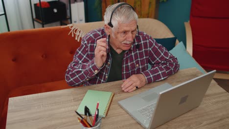Senior-man-freelance-wear-headphone-make-video-call-talking,-teaching-at-laptop-at-home-office